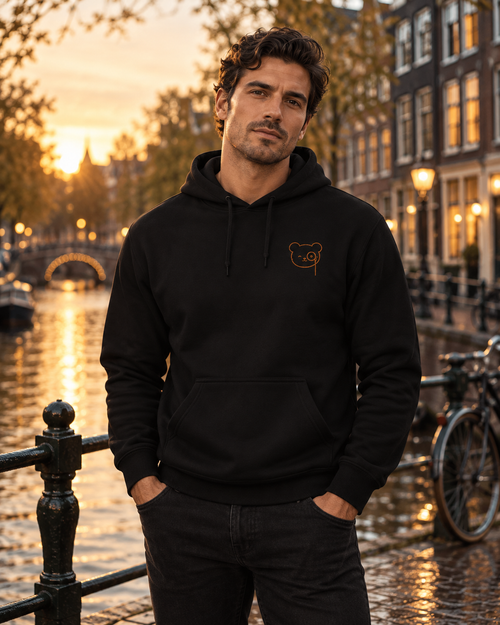 Black pullover hoodie with a small copper Teddy O’Broin bear-face emblem printed on the left chest.