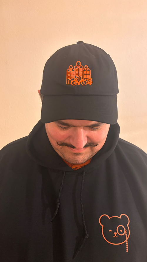 Man wearing the black Amsterdam City Lines dad hat with orange canal house and bicycle embroidery